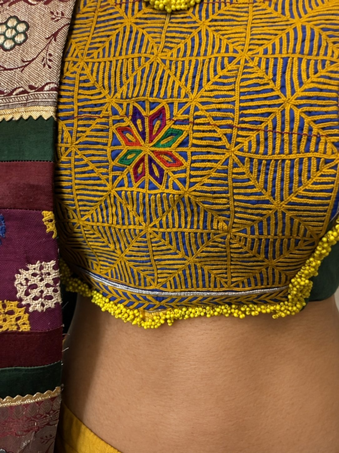 Close view of the embroidered blouse patch and yellow beaded hem