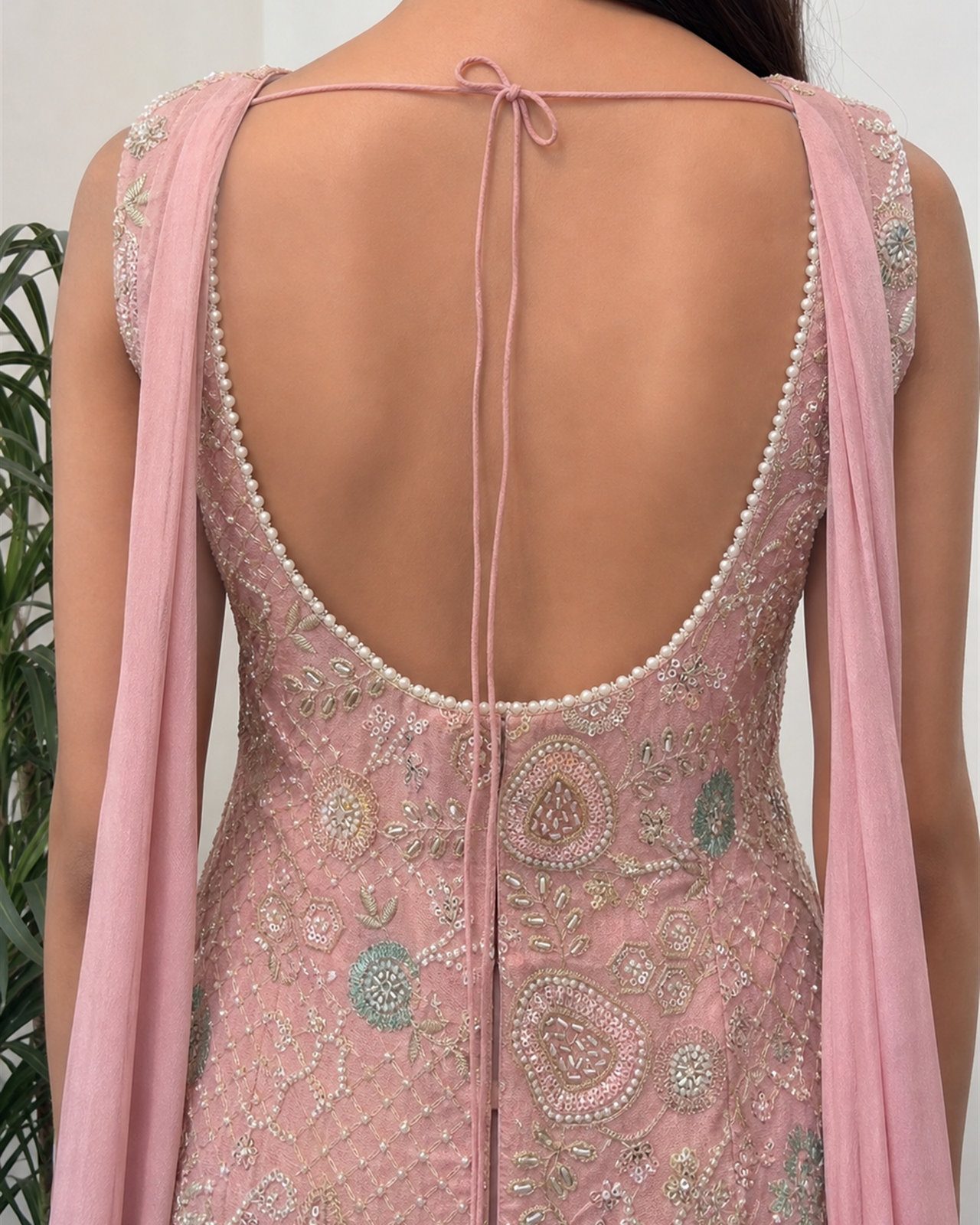 Close view of the pink tissue top, pearl-edged open back with tie cord and draped panels